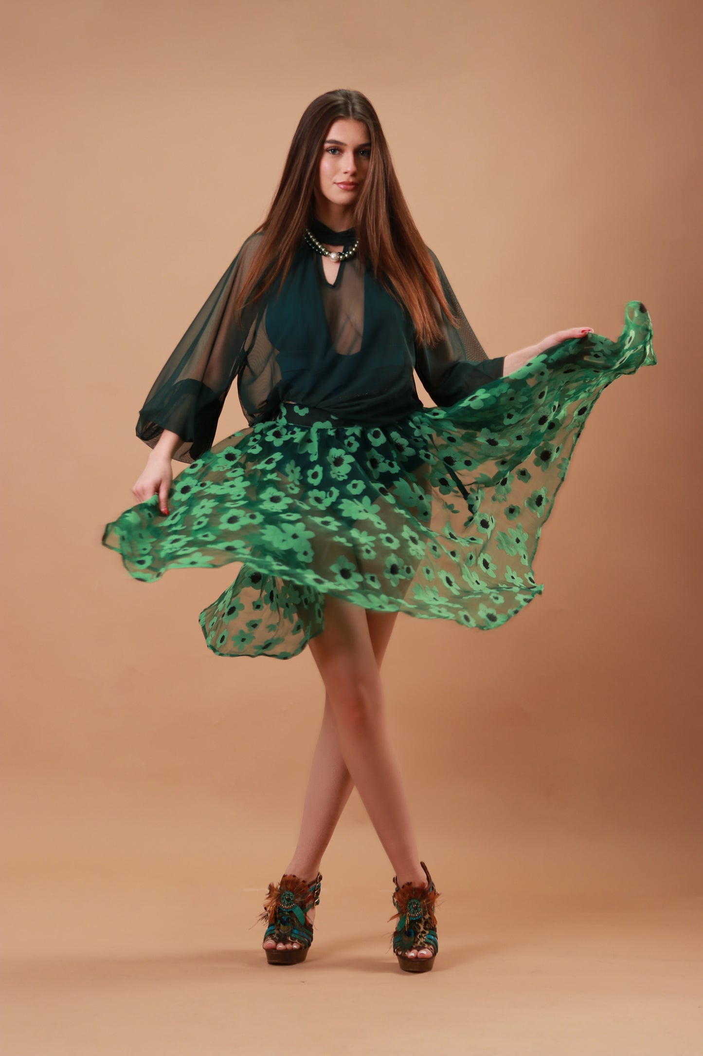 Woman wearing a green see-through skirt with a jungle green swimsuit against a beige background