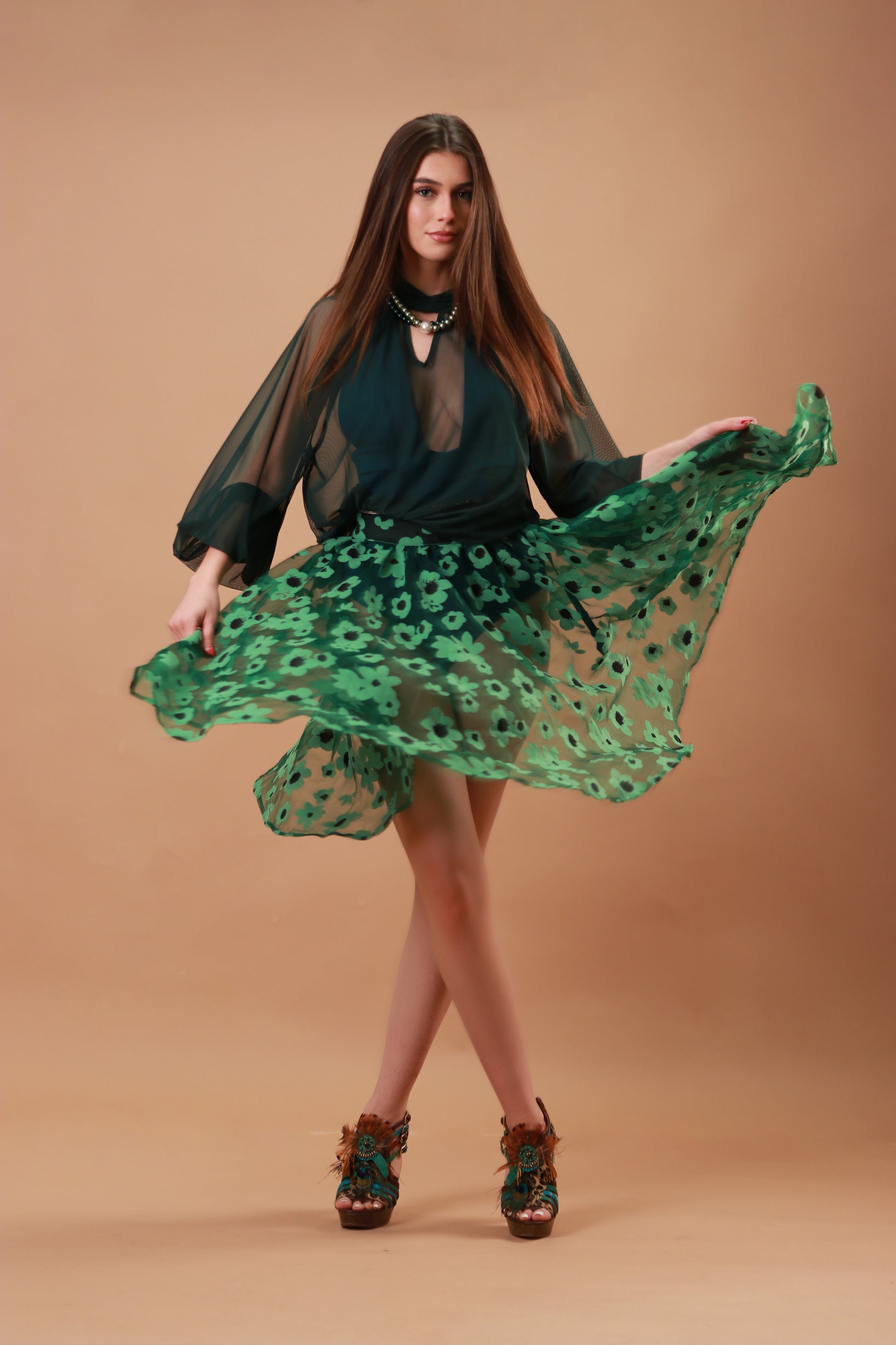 Woman wearing a green see-through skirt with a jungle green swimsuit against a beige background