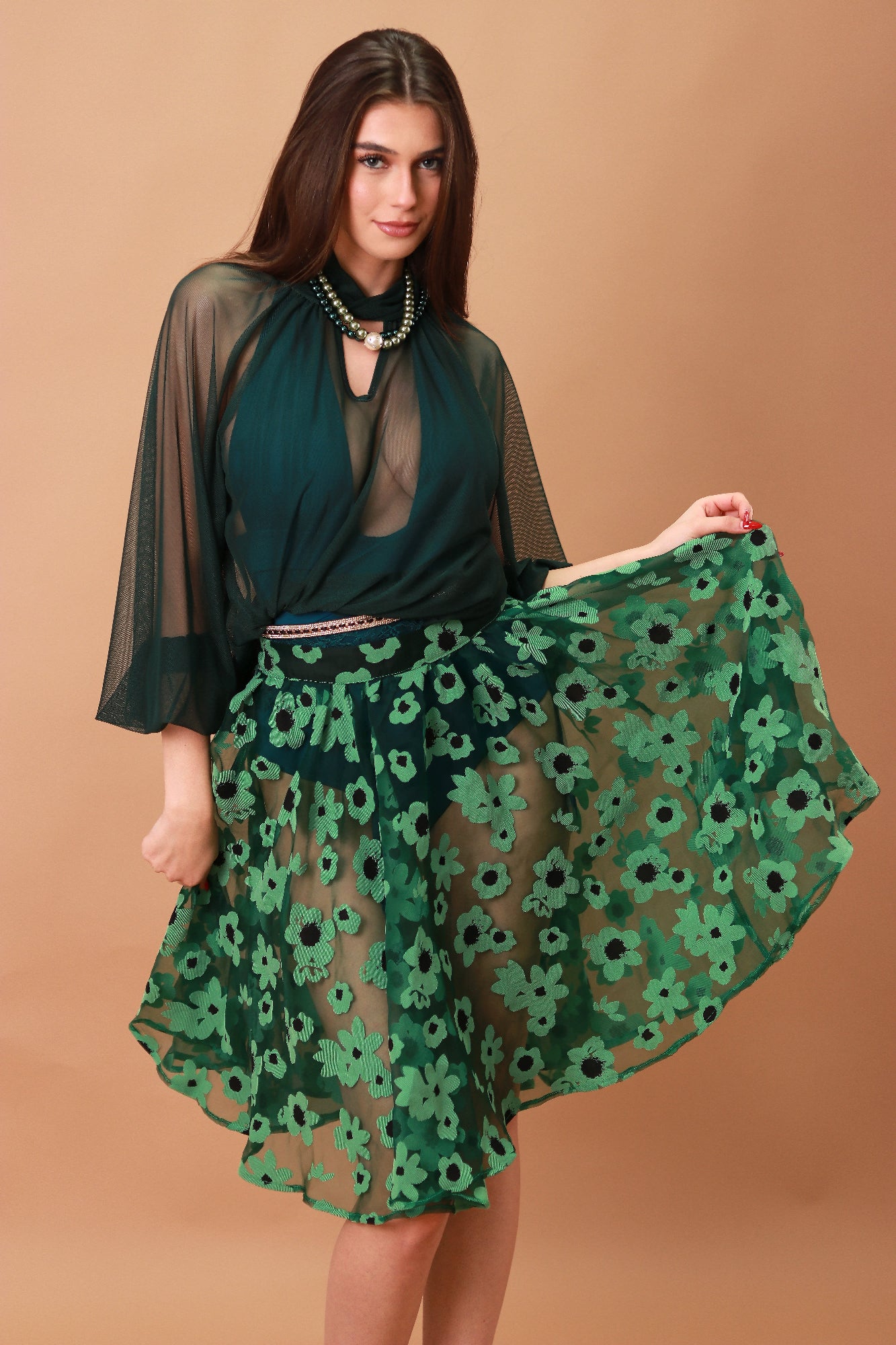 Woman wearing a green floral skirt and sheer top against a brown background