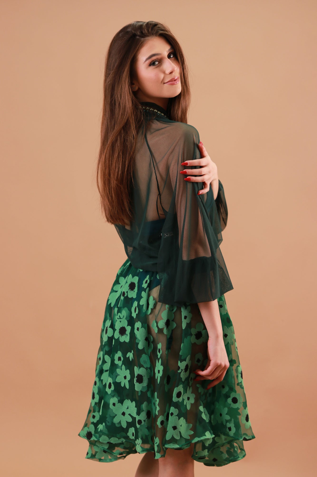 Woman wearing a green floral skirt with green blouse against a beige background