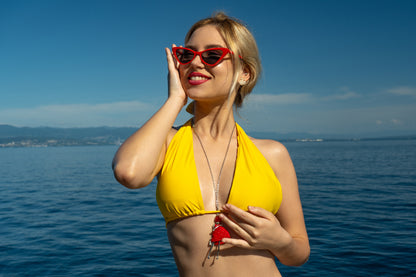 Model in the Volosko Sunset bikini top in Yellow Sun standing on a yacht with the panorama of the Adriatic sea
