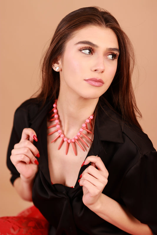 Woman wearing a black top and pink necklace against a beige background